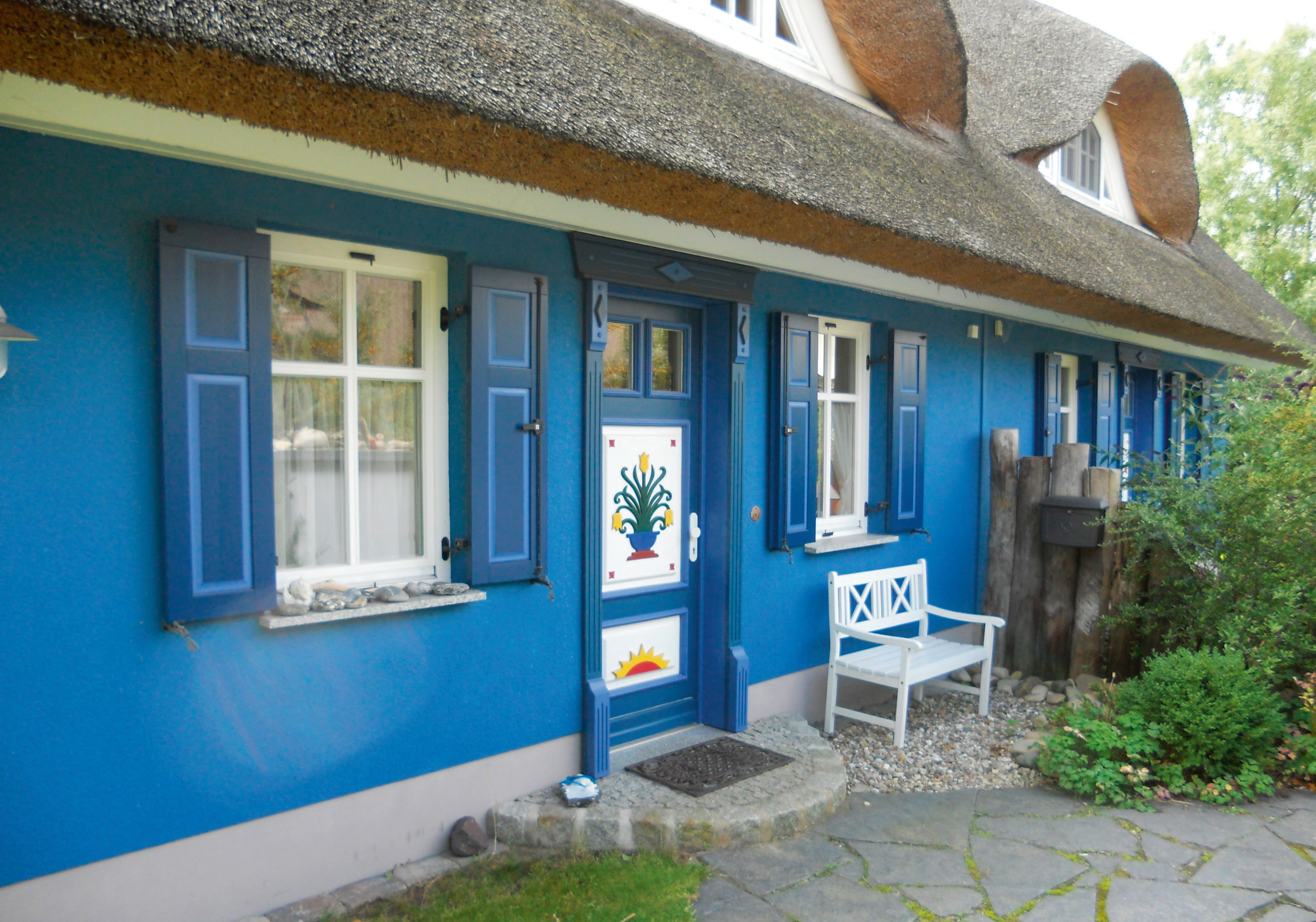 Blaue Hausfassade mit Sprossenfenster, Fensterläden und Rohrdach